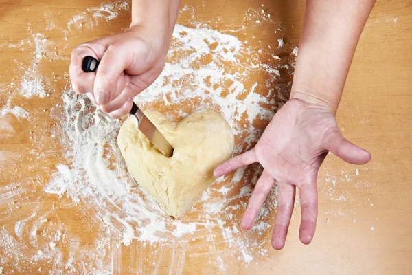 Nervous woman pierces heart of dough with kitchen knife — Stock Photo, Image