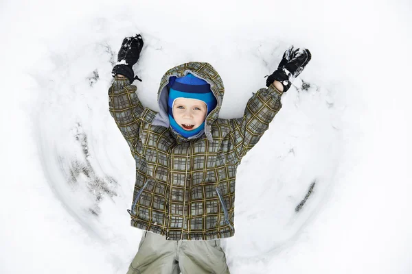 Pequeño niño yace en la nieve y jugando — Foto de Stock