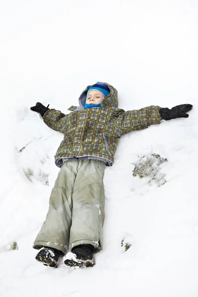 Llittle pojke ligger på snö och spela — Stockfoto