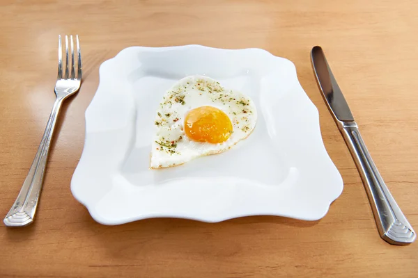 Fried eggs in a heart shape on a white plate and cutlery — Stock Photo, Image