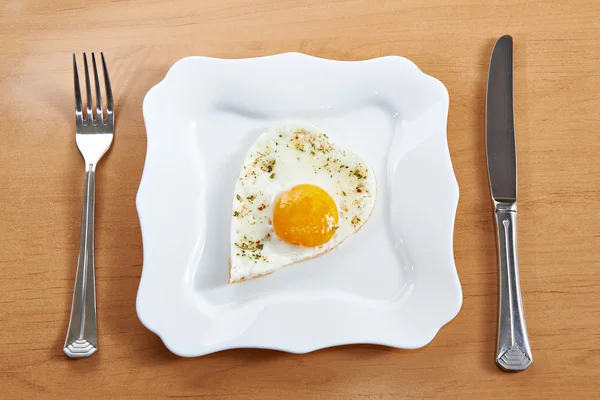 Смажені яйця у формі серця на білій тарілці та столові прибори — стокове фото