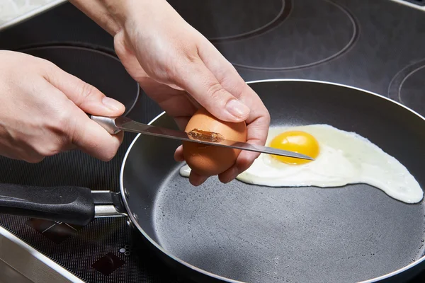 Femme casse un œuf dans des œufs frits avec un couteau — Photo