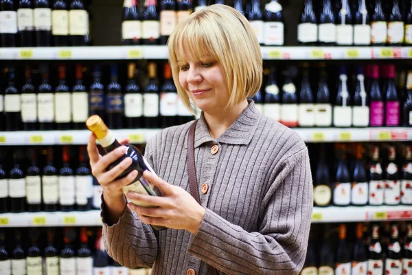 Vrouw leest etiket op een fles wijn in winkel — Stockfoto