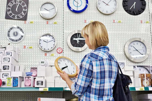 Woman chooses wall clock in store — Stock Photo, Image