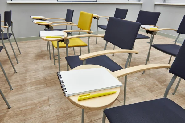 Chaises avec bloc-notes dans une salle de classe vide — Photo