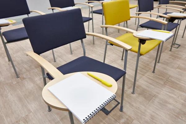 Chaises avec bloc-notes dans une salle de classe vide — Photo