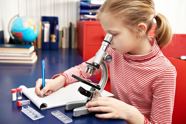 Chica utiliza un microscopio y escribe resultados — Foto de Stock