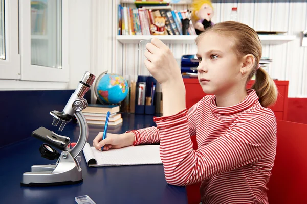 Meisje maakt gebruik van een microscoop en schrijft resultaten — Stockfoto