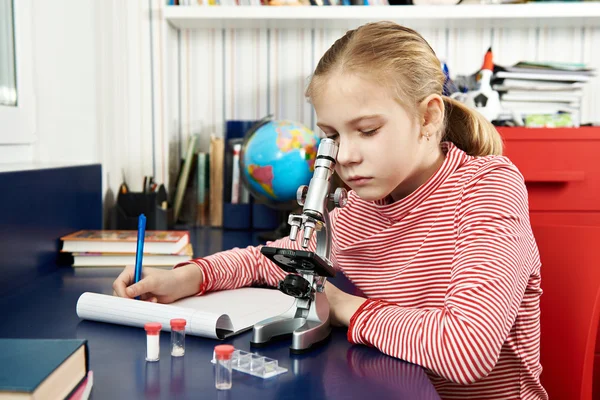 Chica utiliza un microscopio y escribe resultados — Foto de Stock