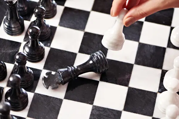 Hand with white pawn hits black king — Stock Photo, Image