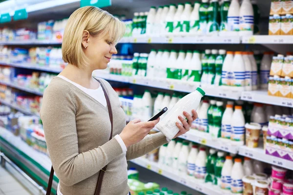 Vrouw met mobiele telefoon winkelen melk — Stockfoto