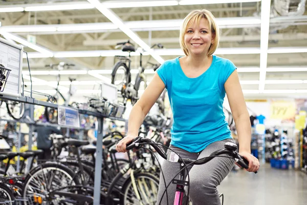 Atractiva bicicleta de prueba de mujer atlética en la tienda —  Fotos de Stock