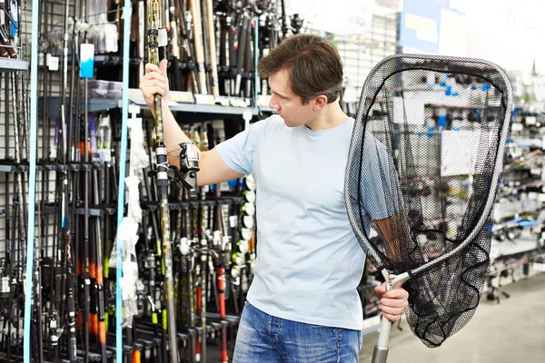 Man chooses fishing rod and landing net in sports shop — Stock Photo, Image