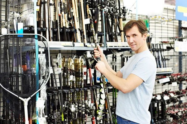 Man chooses fishing rod in sports shop — Stock Photo, Image