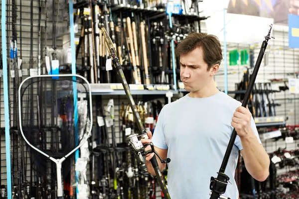 Hombre elige caña de pescar en tienda de deportes —  Fotos de Stock