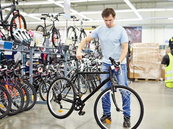 Hombre comprueba bicicleta antes de comprar en tienda de deportes —  Fotos de Stock