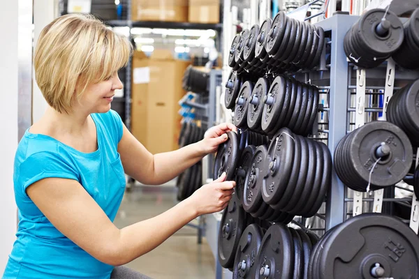 Happy woman chooses loads for dumbbell in sports shop — Stock Photo, Image