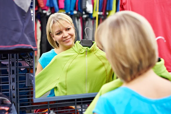 Mujer feliz cerca del espejo tratando de ropa deportiva en la tienda — Foto de Stock