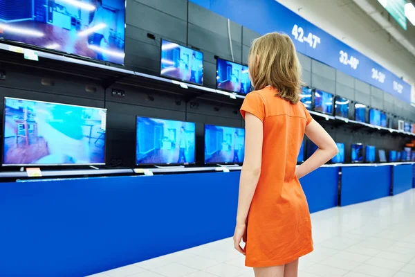 Teenager girl looks at LCD TVs in shop — Stock Photo, Image