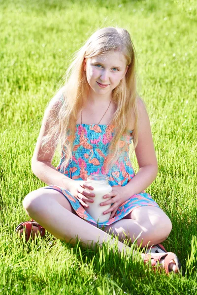 Mädchen sitzt mit einem Krug Milch auf der Wiese — Stockfoto