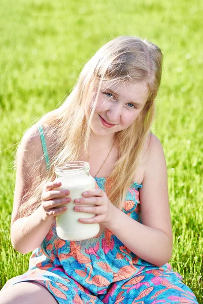 Meisje zit in de weide met een kruik van melk — Stockfoto