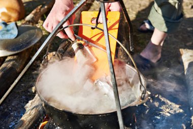 Cooking fish soup in the stowed bowler over campfire clipart