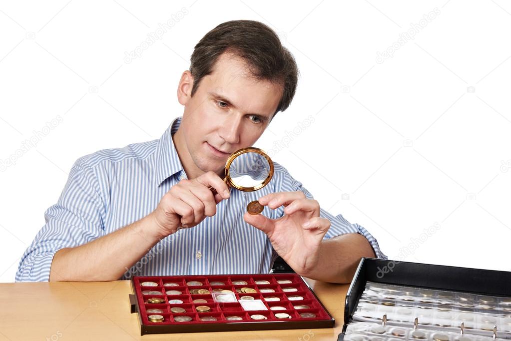 Man numismatist examines coin with magnifying glass Stock Photo by