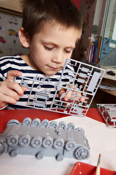 Little boy collects plastic model tank — Stock Photo, Image