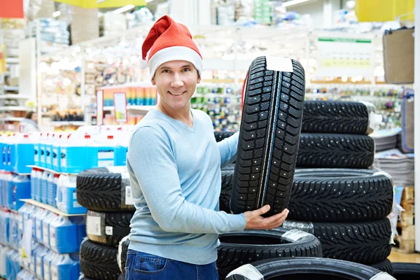 Hombre feliz en Santa sombrero con neumáticos de invierno de regalo en la tienda de Navidad — Foto de Stock