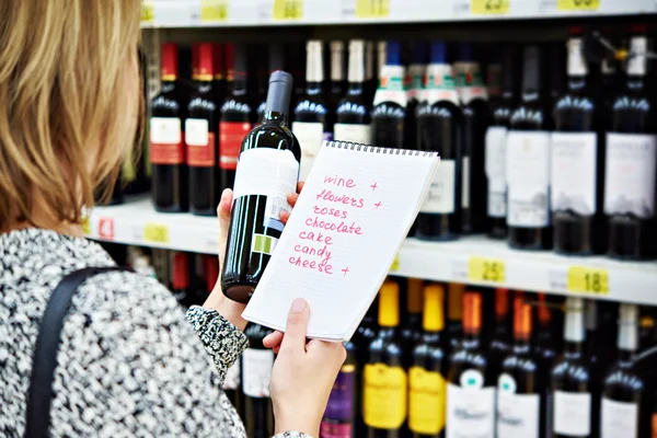 Meisje kiest fles wijn voor datum in winkel — Stockfoto