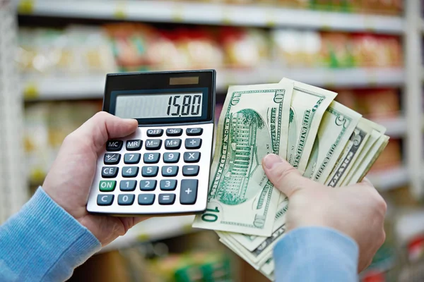 Man with dollars and calculator considers costs in store — Stock Photo, Image