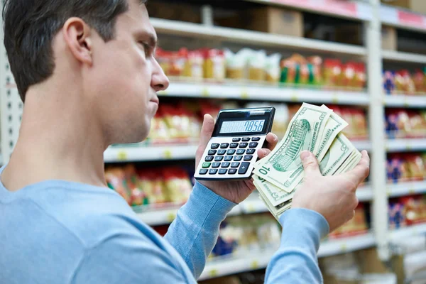 Man with dollars and calculator considers costs in store — Stock Photo, Image