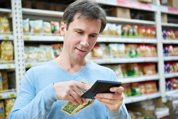 Man with dollars and calculator considers costs in store — Stock Photo, Image