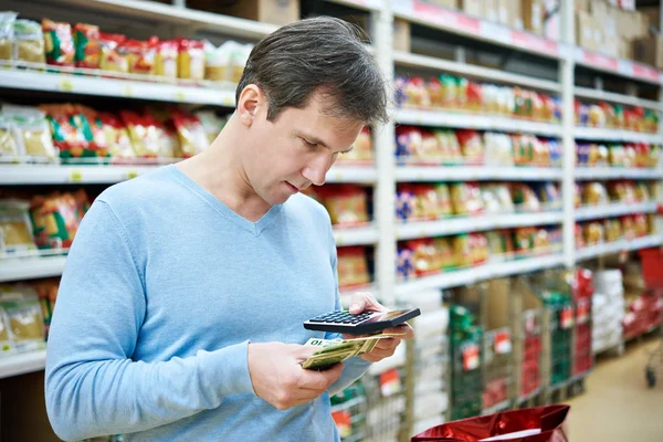 Hombre con dólares y calculadora considera los costos en la tienda — Foto de Stock