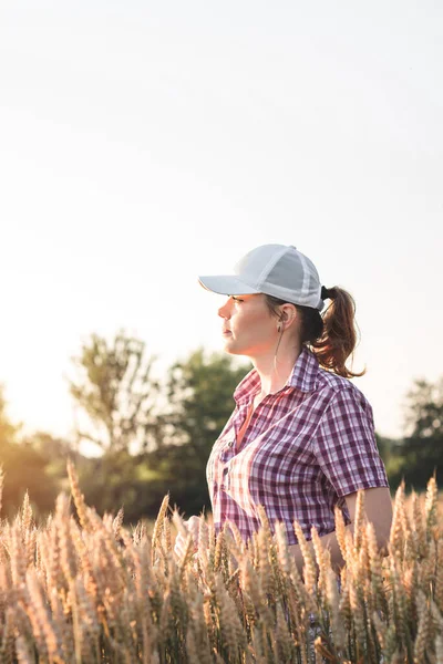 Young woman farmer works on a wheat field in the sun. Business woman plans her income in the field. Female agronomist with a tablet study the wheat crop in the agricultural field. Grain harvest.