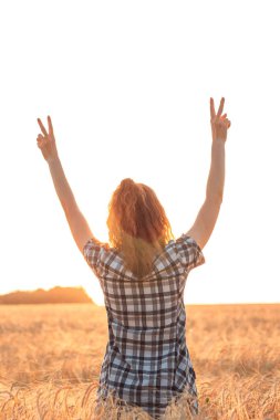 Gün batımında buğday tarlasında kollarını açmış bir kız.