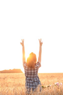 Gün batımında buğday tarlasında kollarını açmış bir kız.