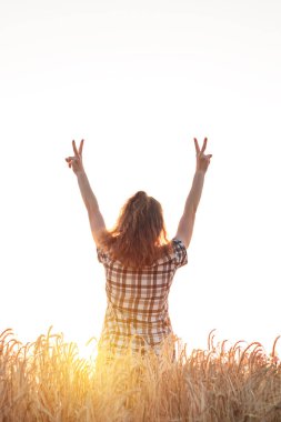 Gün batımında buğday tarlasında kollarını açmış bir kız.