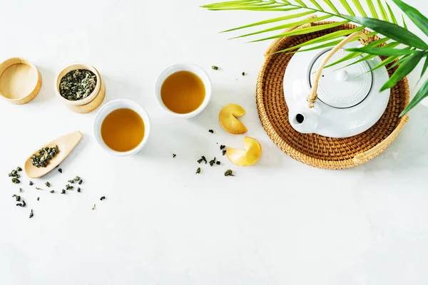 アジア茶の概念の上から見ると 薄い背景に乾燥した緑茶で囲まれた2つの白いカップ フォーチュンクッキー ティーポット — ストック写真