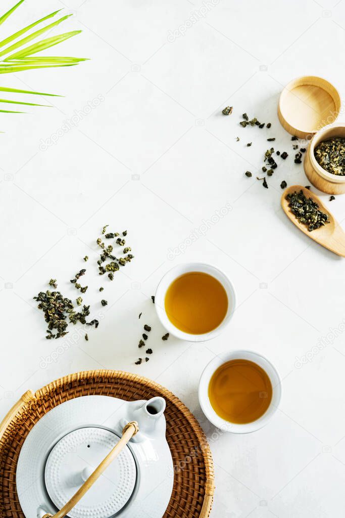 Asian tea concept, two white cups of tea and teapot surrounded with green tea dry leaves view from above, space for a text on white background