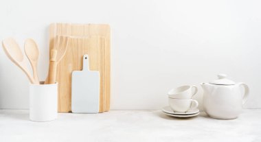 Mutfak arka planında çay demliği ve yemek pişirme aletleri merdane, kesme tahtası, beyaz arka plandaki masada kaseler. Mesaj atmak için boş bir alan, mutfak dekorasyonu konsepti. Geniş pankart.