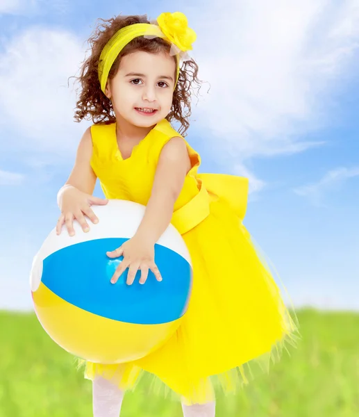 Little girl in yellow dress holding a ball — Stock Photo, Image