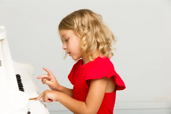 Beautiful little girl is playing on a white grand piano.