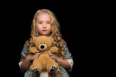 Siyah arka planda oyuncak ayısı olan küçük bir kız..