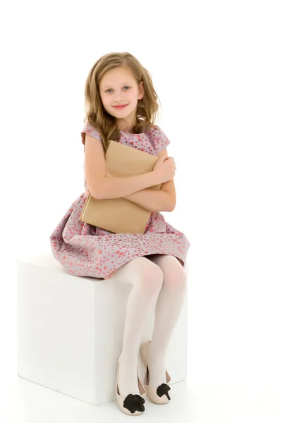 Menina bonita em vestido rosa sentado no cubo branco Segurando Livro — Fotografia de Stock