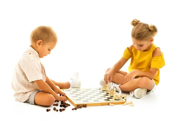 Tenksom liten gutt og liten jente sitter på gulvet og spiller sjakk. – stockfoto