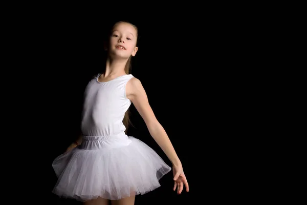 Menina bonito em um tutu e sapatos pontiagudos está dançando no estúdio em um fundo preto. — Fotografia de Stock