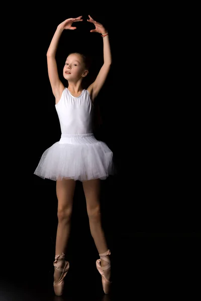 Schattig klein meisje in een tutu en pointe schoenen is dansen in de studio op een zwarte achtergrond. — Stockfoto