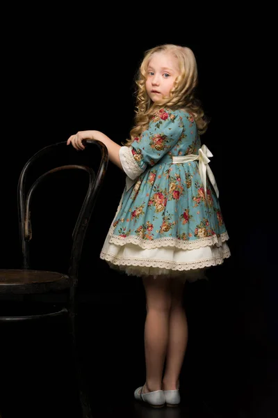 Portret van een meisje op een zwarte achtergrond bij de oude Weense stoel. — Stockfoto