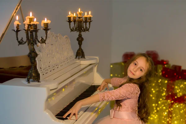 Ragazza in posa mentre seduto al pianoforte decorato con candele ardenti. — Foto Stock